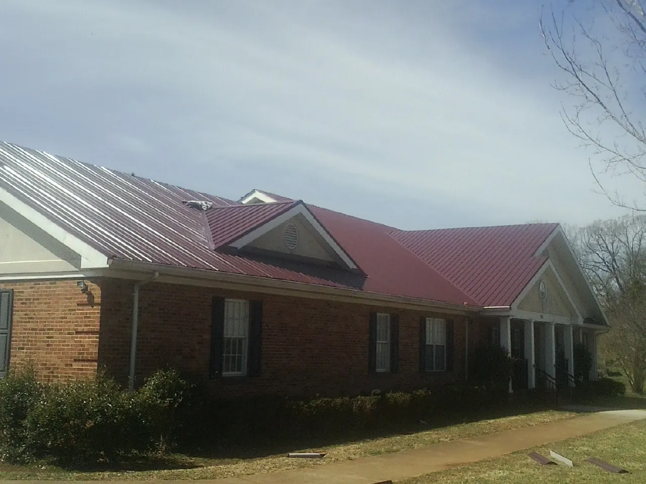 Red metal roof with gabled entries on a long brick building, from a Hail Damage Roof Repair job in West Springfield