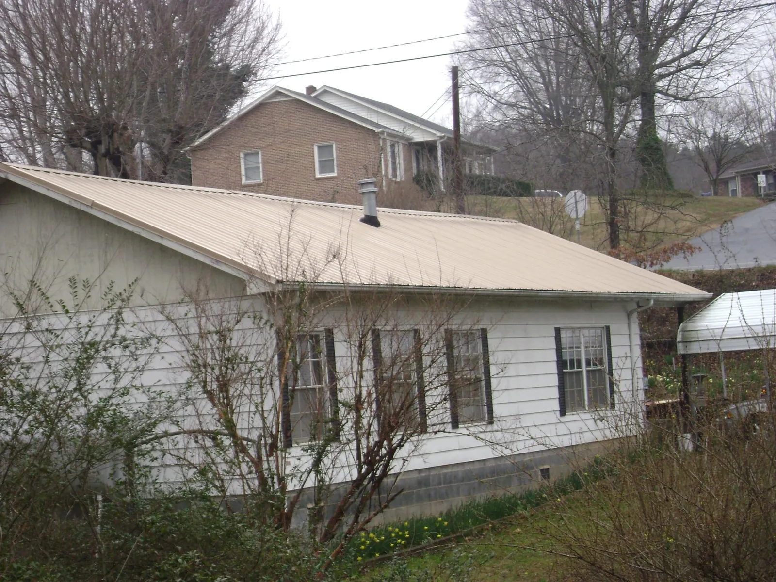Tan metal roof on a white sided house set into a hillside — Commercial Roofing by Roofing Brothers in West Springfield